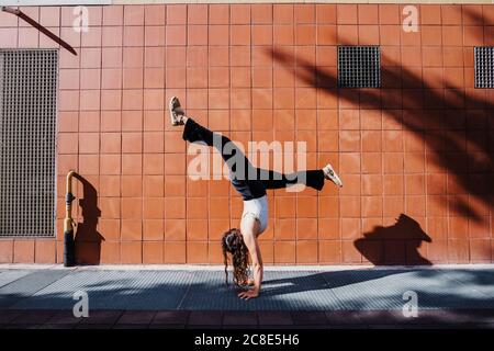 Jeune femme qui exécute la main sur le trottoir contre le mur de carrelage à l'intérieur ville pendant la journée ensoleillée Banque D'Images