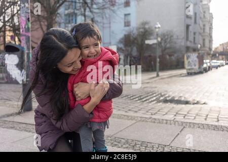 Une femme heureuse embrasse sa fille tout en s'agenouillant sur le sentier ville Banque D'Images