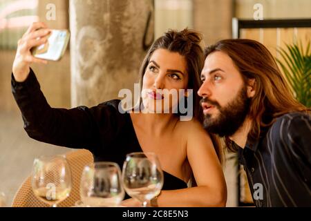 Belle jeune femme prenant selfie avec un ami barbu au restaurant Banque D'Images