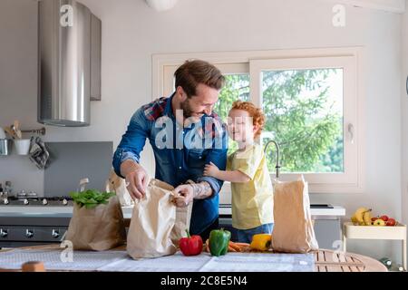 Un père et un fils joyeux avec des articles d'épicerie à la table dans la cuisine Banque D'Images