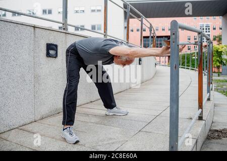 Homme âgé avec les bras relevés fléchissant en se tenant sur la passerelle en ville Banque D'Images