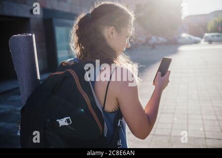 Jeune femme sportive utilisant un smartphone tout en marchant en ville rue pendant la journée ensoleillée Banque D'Images