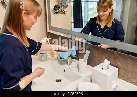 Une femme de chambre souriante qui essuyait le robinet de la salle de bains dans l'hôtel Banque D'Images