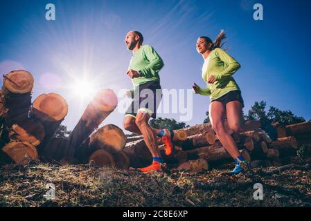 Couple mature qui court sur terre contre ciel dégagé en forêt par beau temps Banque D'Images