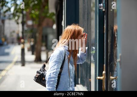 Jeune femme à tête rouge regardant par la fenêtre du magasin dans la ville Banque D'Images