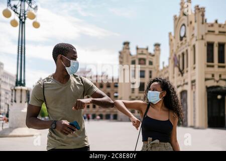 Homme et femme portant des masques tout en saluant l'un l'autre avec coudes en ville Banque D'Images