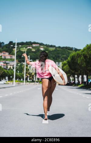Vue arrière de la femme surfeuse marchant avec planche de surf dans la rue Banque D'Images
