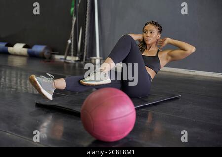 Jeune femme avec les mains derrière la tête faisant un exercice abdominal sur tapis dans la salle de sport Banque D'Images