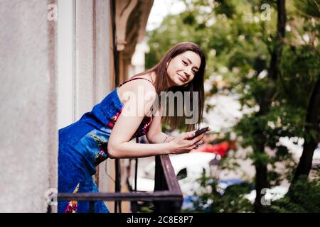 Femme utilisant le téléphone tout en se penchant sur les balustrades de balcon Banque D'Images