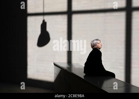 Femme professionnelle vêtue d'un costume noir se détendant sur le mur de maintien avec lumière du soleil et ombre à l'arrière-plan au bureau Banque D'Images