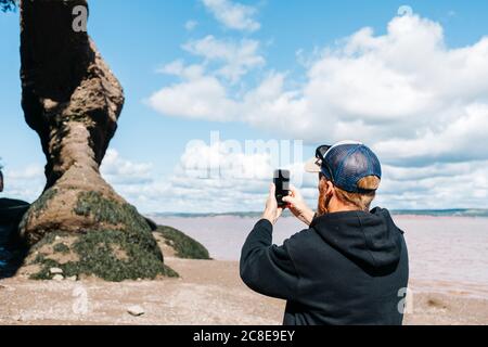 Homme photographiant la formation rocheuse au parc Hopewell Rocks, Nouveau-Brunswick, Canada Banque D'Images