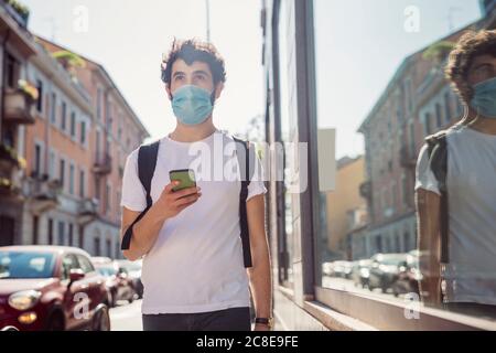 Homme portant un masque tenant un smartphone tout en marchant dans la ville Banque D'Images