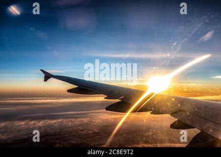 Vue sur l'aile gauche de l'avion passager. Le coucher du soleil se fait sous la forme d'une arche lumineuse dorée au-dessus de l'aile. Les nuages épais sous l'avion sont illuminés par le su doré Banque D'Images