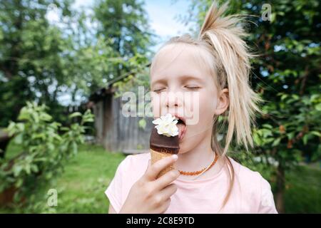 Portrait d'une fille blonde avec les yeux fermés en train de manger de la glace avec fleurs de jasmin dans le jardin Banque D'Images