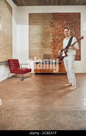 Homme senior jouant de la guitare basse dans un appartement de loft Banque D'Images