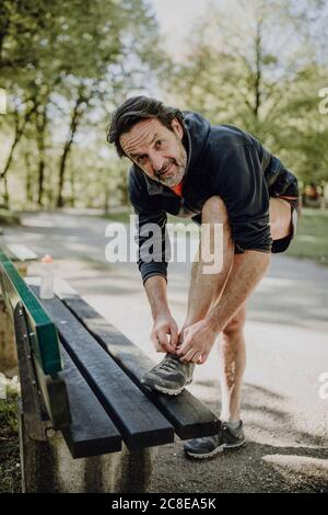 Homme mûr souriant qui noue des lacets sur la paillasse tout en restant debout stationnement Banque D'Images