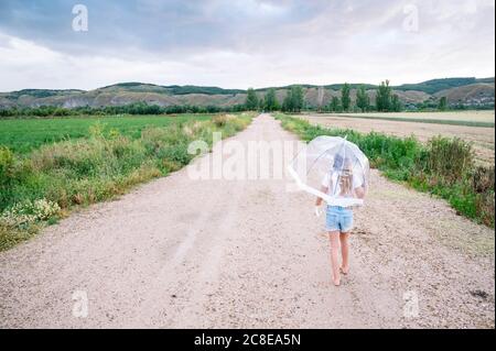 Fille avec parapluie marchant sur la route de terre pendant la mousson Banque D'Images