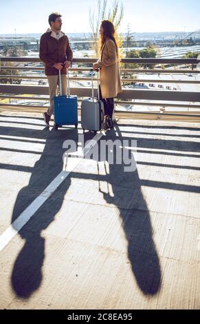 Un couple d'affaires parle en se tenant sur une passerelle surélevée à l'aéroport par beau temps Banque D'Images