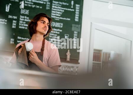 Le barista nettoie la tasse à café en regardant loin tout en se tenant dans le café Banque D'Images