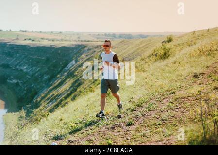 Un jeune homme portant des lunettes de soleil fait du jogging sur une colline par une journée ensoleillée Banque D'Images