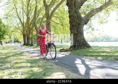 Femme attentionnés marchant avec un vélo sur la piste de marche dans le parc public Banque D'Images