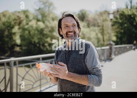 Homme souriant tenant une bouteille d'eau tout en se tenant sur la passerelle stationnement Banque D'Images