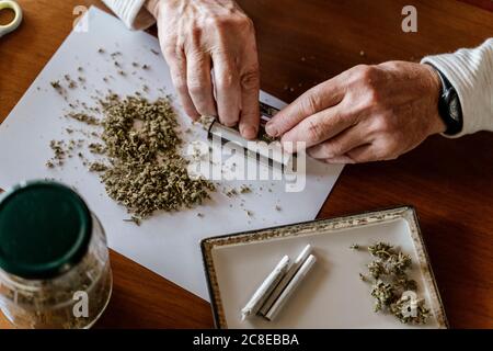 Vue en grand angle de l'homme qui roule des mauvaises herbes sur la table à la maison Banque D'Images