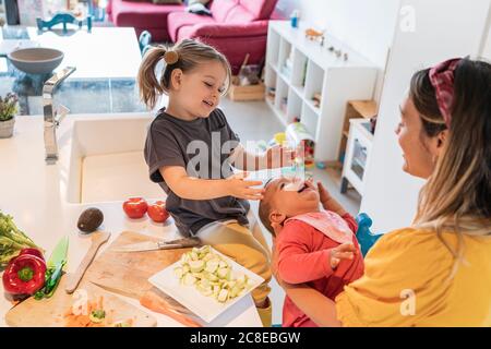 Bonne mère et fille jouant avec bébé fille dans la cuisine à la maison Banque D'Images