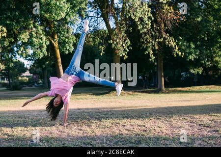 Fille faisant cartwheel sur la terre contre les arbres dans le parc Banque D'Images