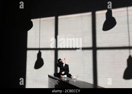 Femme professionnelle vêtue d'un élégant costume reposant sur un mur de maintien avec lumière du soleil et ombre en arrière-plan Banque D'Images