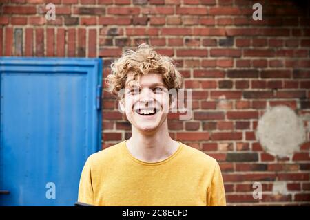 Portrait d'un jeune homme aux cheveux blonds bouclés devant de mur de brique Banque D'Images