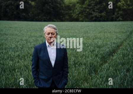 Portrait d'un homme d'affaires senior avec les yeux fermés sur un champ à la campagne Banque D'Images