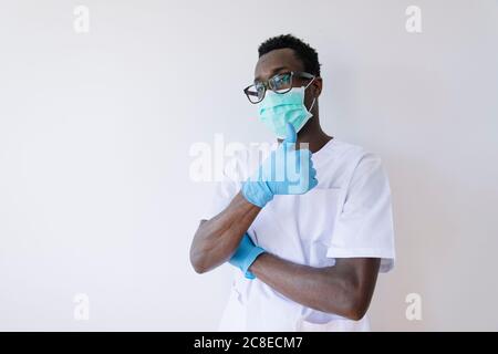 Médecin afro portant un masque chirurgical montrant les pouces debout sur fond blanc Banque D'Images