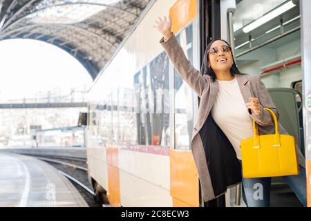 Jeune femme élégante portant des lunettes de soleil se portant à la main tout en se tenant debout entrée du train Banque D'Images