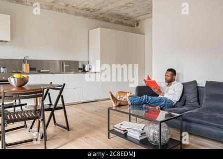 Homme assis sur un canapé dans un appartement moderne lisant un livre Banque D'Images