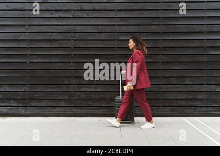 Jeune femme professionnelle marchant avec des bagages sur la piste de marche en noir mur en bois en ville Banque D'Images