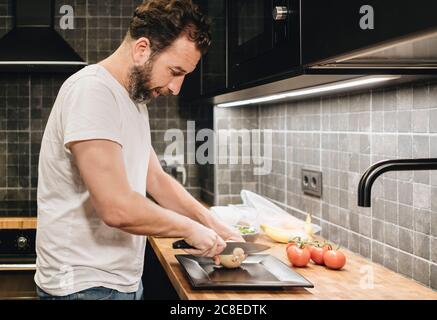 Homme mûr debout dans la cuisine, hacher des oignons Banque D'Images