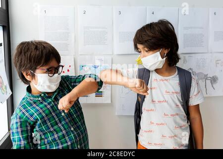 Les écoliers portent des masques donnant une bosse de coude tout en se tenant contre le mur à l'école Banque D'Images