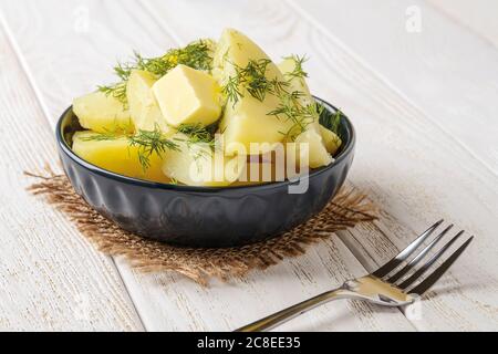 De délicieuses pommes de terre fraîchement cuites avec du beurre fondu et de l'aneth dans un bol en céramique sur une table en bois blanc. Cuisez à la maison un délicieux plat de légumes. Banque D'Images