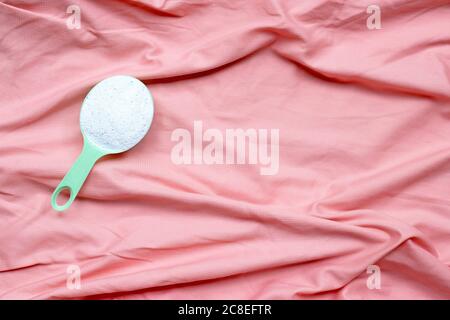 Lessive en poudre dans une cuillère de mesure dans un chiffon rose avant le lavage. Concept de blanchisserie. Banque D'Images