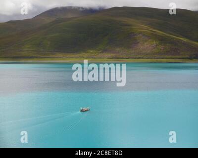 Le bateau sur le lac vert se dirigeant vers la montagne loin. La photo a été prise au Tibet Banque D'Images