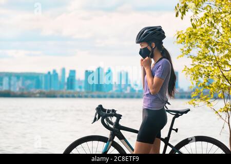 Porter un masque Covid-19 en vélo. Sport cycliste femme vélo mettant sur masque pour la prévention Covid-19 pendant l'été loisirs en plein air Banque D'Images