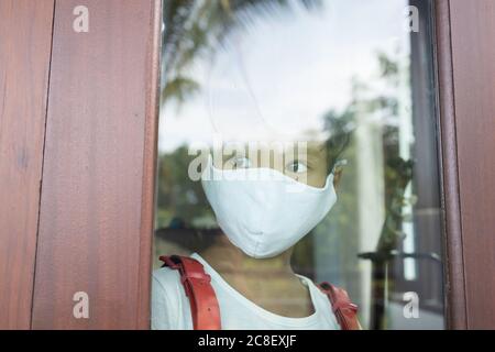 Une fille asiatique d'école élémentaire portant un masque est dans une humeur triste à la fenêtre. L'image montre l'idée pendant la quarantaine à domicile pour réduire la propagation Banque D'Images