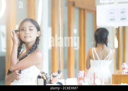 Une jeune fille asiatique aux cheveux longs utilise une brosse à cils pendant la leçon de maquillage. Banque D'Images