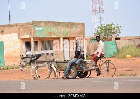 Un cycliste hcette un tour d'une carette d'âne passant dans un village africain Banque D'Images