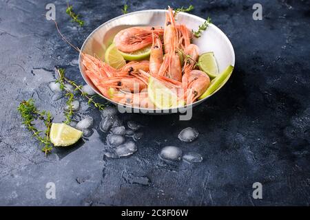 Grandes crevettes fraîches à la chaux, branches de razmarin, glace sur fond sombre, gros plan. Fruits de mer, aliments sains Banque D'Images