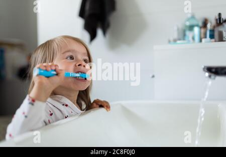 Bébé fille dans la salle de bains lumineuse se brossant les dents au-dessus de l'évier. Banque D'Images