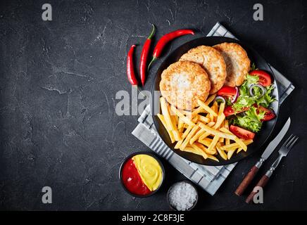 hamburgers de dinde frits servis avec salade de tomates et frites sur une assiette noire sur une table en béton, avec ketchup et moutarde vue horizontale Banque D'Images