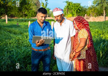 Jeune indien avec ordinateur portable montrant quelque chose à la famille paysanne de village sur Internet debout dans le champ vert, la terre agricole, l'ordinateur d'enseignement et u Banque D'Images