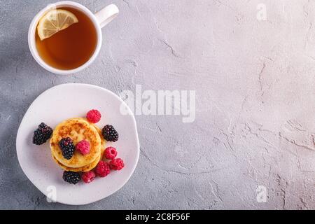 Crêpes au fromage cottage, beignets de caillé dessert aux framboises et aux mûres dans un plat près d'une tasse de thé chaud avec une tranche de citron Banque D'Images